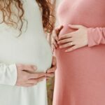 Two expectant women gently holding their pregnant bellies, symbolizing motherhood and maternity.